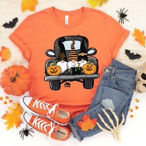 May include: Orange t-shirt with a graphic of three gnomes in a black truck with pumpkins and a cauldron. The gnomes are wearing black hats and have white beards. The truck has a spider web on the back.
