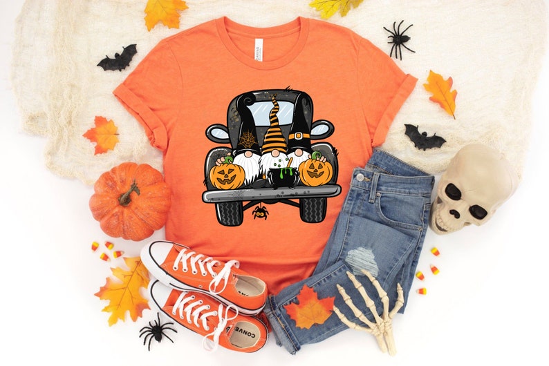 May include: Orange t-shirt with a graphic of three gnomes in a black truck with pumpkins and a cauldron. The gnomes are wearing black hats and have white beards. The truck has a spider web on the back.