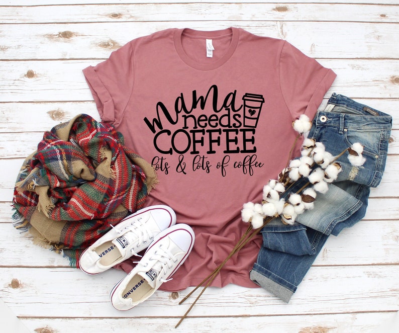 Puede incluir: Una camiseta color malva con el texto "mama needs coffee lots & lots of coffee" en letras negras. Un icono de taza de caf&eacute; est&aacute; al lado de la palabra "coffee".