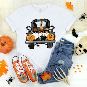 May include: White t-shirt with a graphic of three gnomes riding in the back of a black pickup truck. The gnomes are wearing Halloween costumes and holding pumpkins. The truck has a cauldron in the bed.