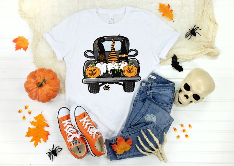 May include: White t-shirt with a graphic of three gnomes riding in the back of a black pickup truck. The gnomes are wearing Halloween costumes and holding pumpkins. The truck has a cauldron in the bed.