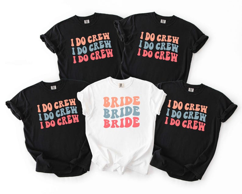 Puede incluir: Cinco camisetas, cuatro negras y una blanca, con texto retro. Las camisetas negras dicen "I DO CREW" en naranja, azul y rosa. La camiseta blanca dice "BRIDE" en los mismos colores. Todas las camisetas tienen mangas cortas.