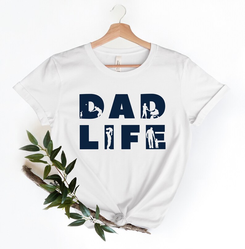 May include: White t-shirt with the text "DAD LIFE" in navy blue. The letters are filled with silhouettes of a father interacting with his children.