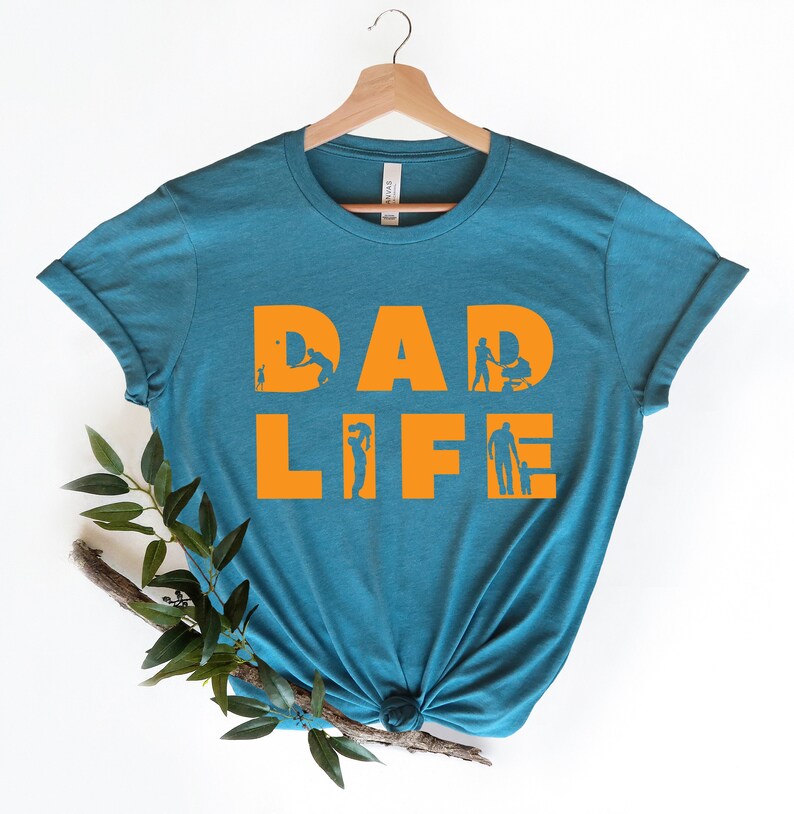 May include: A teal blue t-shirt with the text "DAD LIFE" in orange. The letters are made up of silhouettes of a father doing various activities with his children.