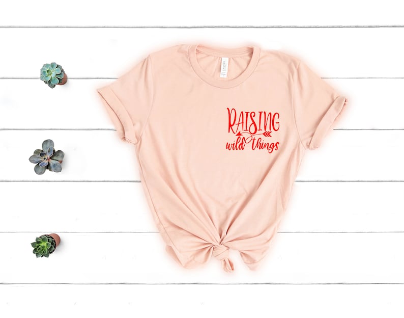 May include: A light pink t-shirt with the text "Raising wild things" in red lettering on the front.