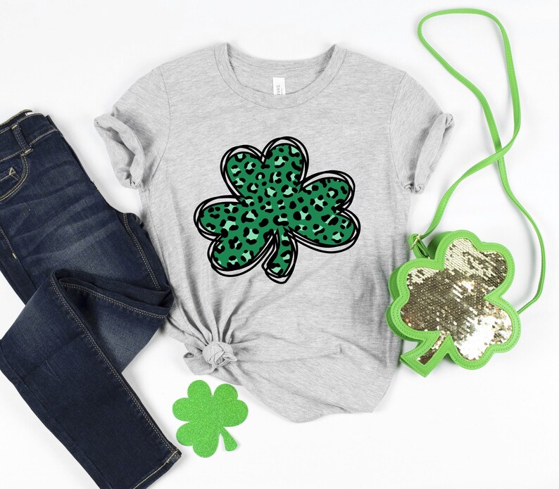 May include: A gray t-shirt with a green shamrock design. The shamrock is made up of leopard print spots.