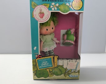 May include: Lime Chiffon Strawberry Shortcake doll with a green parrot and a comb. The doll has green hair, a green dress, and green and white striped stockings. The box is pink and blue with a picture of a lime and a strawberry.