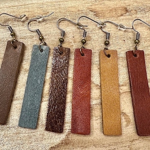 May include: Five pairs of leather earrings with different colored leather strips. The earrings are all made with a simple design and have a rustic look.