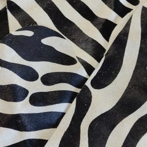 May include: Close-up of a black and white zebra print rug. The rug has a soft, fuzzy texture and is made of natural materials.