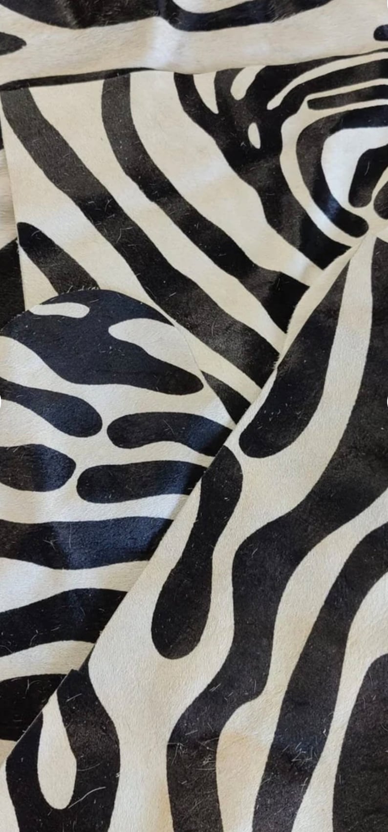 May include: Close-up of a black and white zebra print rug. The rug has a soft, fuzzy texture and is made of natural materials.