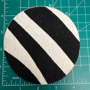 May include: A round, black and white zebra-print coaster. The coaster is made of a soft, fuzzy material.