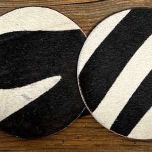 May include: Four round black and white coasters with different zebra-like patterns.