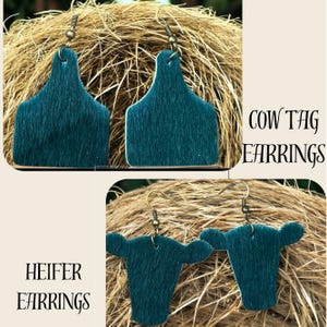 May include: Teal-colored cow tag earrings and heifer earrings with a textured finish. The earrings are displayed against a backdrop of woven brown material. The words "COW TAG EARRINGS" and "HEIFER EARRINGS" are printed on the image.