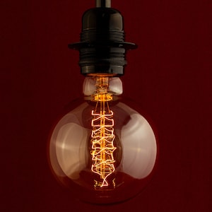 May include: A clear glass light bulb with a coiled filament glowing inside. The bulb is attached to a black metal socket.