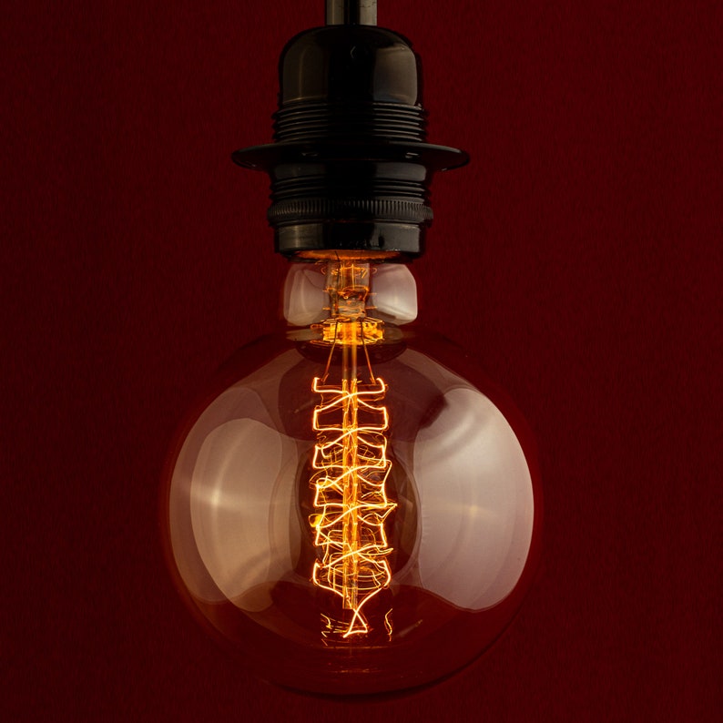 May include: A clear glass light bulb with a coiled filament glowing inside. The bulb is attached to a black metal socket.