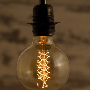 May include: A clear glass light bulb with a decorative filament in the shape of a spiral. The bulb is hanging from a black metal fixture.
