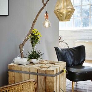 May include: A wooden table made of stacked planks is decorated with a branch with a light bulb hanging from it. A potted plant and a vase of yellow flowers are on the table. A black leather chair is in the background.