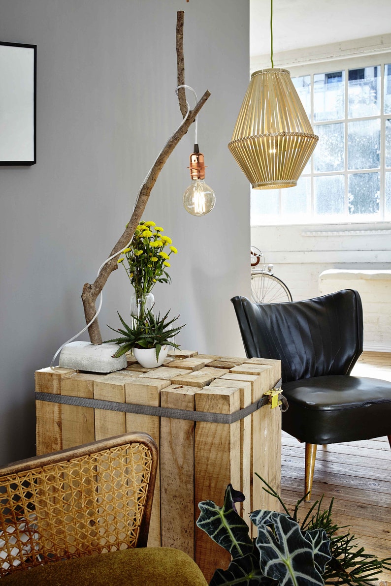 May include: A wooden table made of stacked planks is decorated with a branch with a light bulb hanging from it. A potted plant and a vase of yellow flowers are on the table. A black leather chair is in the background.