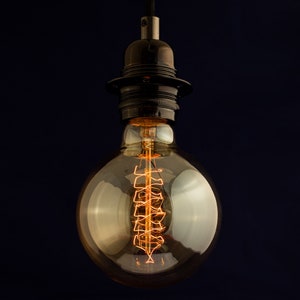 May include: A vintage-style light bulb with a coiled filament, hanging from a black metal socket. The bulb is clear glass and emits a warm, orange glow.