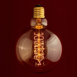 May include: A clear glass light bulb with a gold metal base and a coiled filament inside. The bulb is lit and glowing orange.