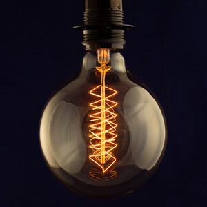 May include: A clear glass light bulb with a coiled filament glowing orange against a dark blue background.