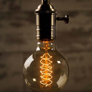 May include: A vintage-style light bulb with a clear glass globe and a coiled filament. The bulb is lit and glowing, casting a warm, yellow light. The bulb is attached to a brass socket with a switch.