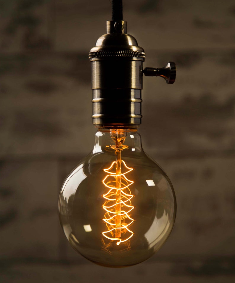 May include: A vintage-style light bulb with a clear glass globe and a coiled filament. The bulb is lit and glowing, casting a warm, yellow light. The bulb is attached to a brass socket with a switch.
