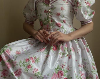 May include: A white dress with a floral print and puffed sleeves. The dress has a square neckline and a pearl necklace.