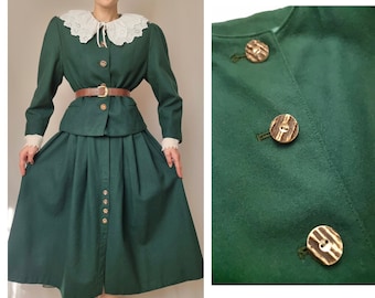 May include: A green skirt and jacket set with a white lace collar. The jacket has a brown belt and the skirt has wooden buttons.
