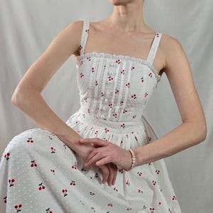 May include: A white midi dress with a cherry print and a lace trim. The dress has a fitted bodice and a full skirt.