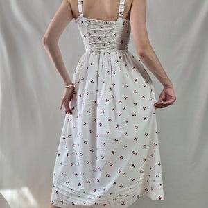 May include: White midi dress with a cherry print and a lace-up back.
