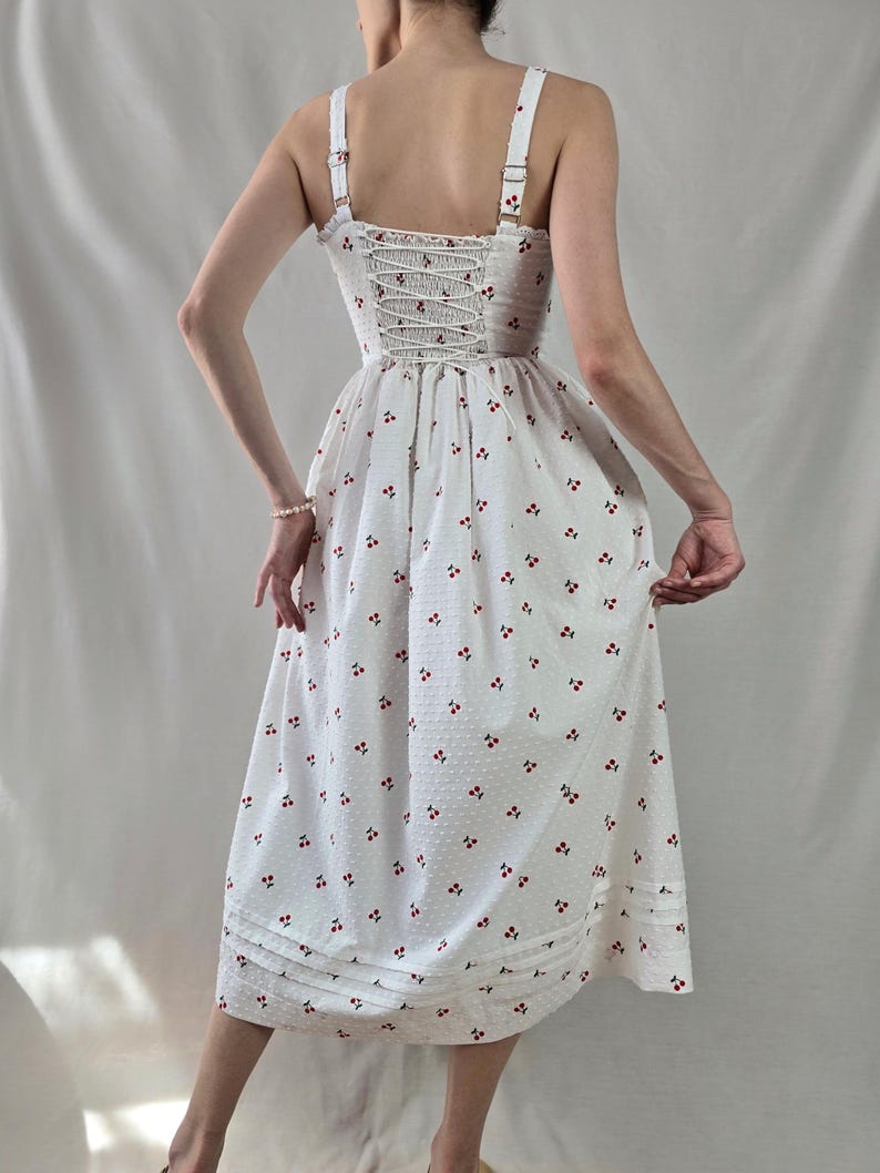 May include: White midi dress with a cherry print and a lace-up back.