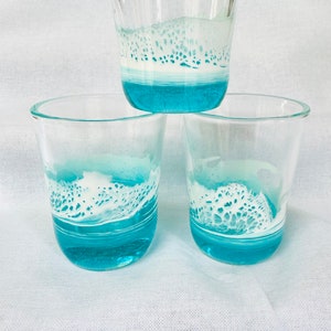 May include: Three clear glass tumblers with a turquoise blue and white design. The design resembles a wave with white foam.