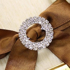 Peut inclure: Un ruban de satin marron noué en un nœud avec une boucle ronde en strass argentés.