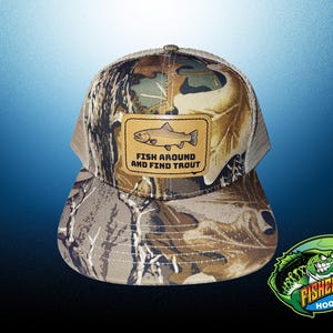 May include: Camouflage baseball cap with a brown leather patch featuring a trout illustration and the text "FISH AROUND AND FIND TROUT." The cap has a mesh back and a curved brim. A logo for "The Fisherman's Hook Up" is in the bottom right corner.
