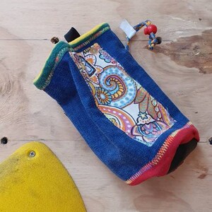 May include: A blue, red, and yellow drawstring bag with a paisley pattern. The bag is made of a soft, durable fabric and has a drawstring closure.
