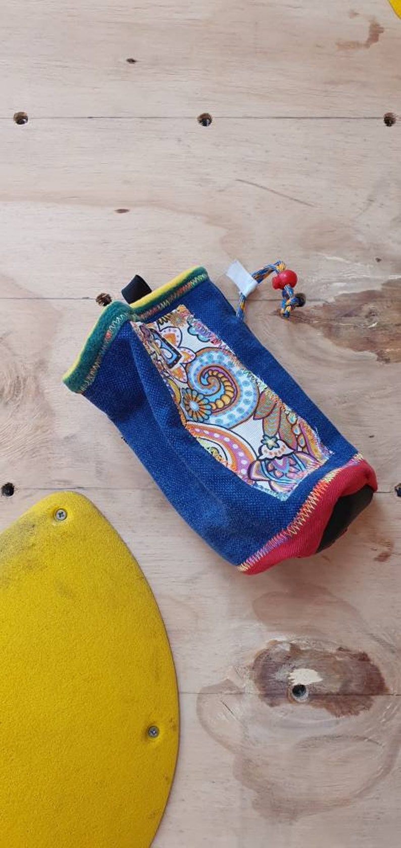 May include: A blue, red, and yellow drawstring bag with a paisley pattern. The bag is made of a soft, durable fabric and has a drawstring closure.
