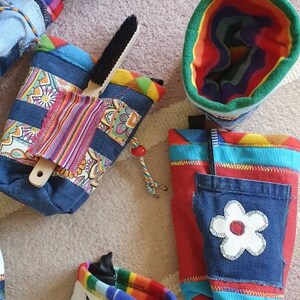 May include: Assortment of colorful fabric pouches with various patterns and designs. Some pouches feature denim fabric, while others have a rainbow pattern. One pouch has a white flower applique.