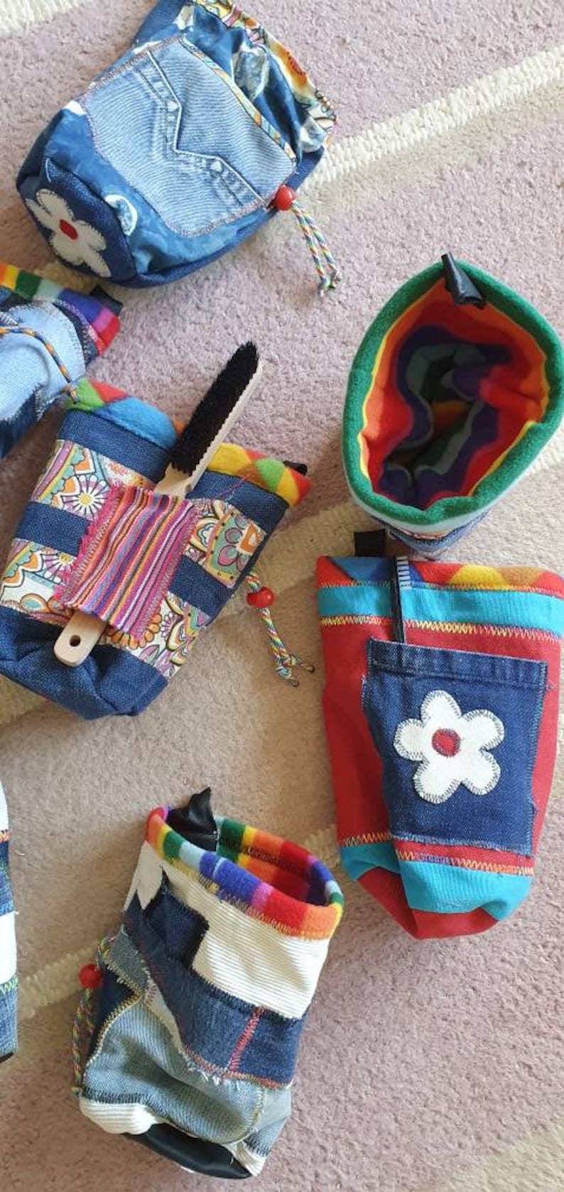 May include: Assortment of colorful fabric pouches with various patterns and designs. Some pouches feature denim fabric, while others have a rainbow pattern. One pouch has a white flower applique.