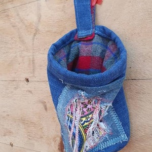 May include: A blue denim pouch with a red and black plaid lining. The pouch has a loop handle and a patch of colorful fabric sewn on the front.