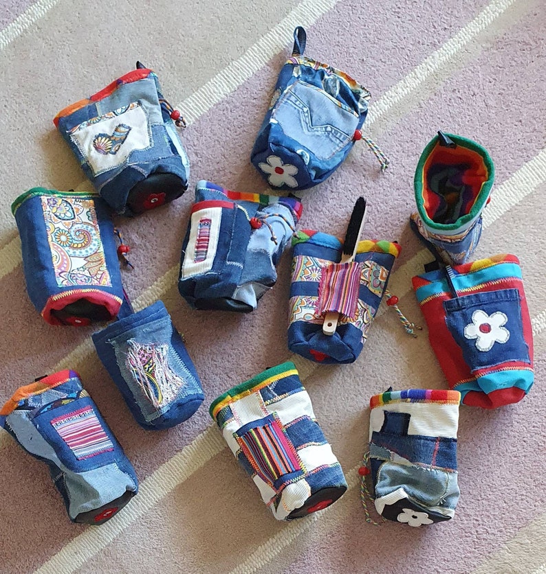 May include: Assortment of colorful fabric drawstring bags with various patterns and designs. The bags are made from recycled denim and feature unique details like embroidered flowers and hearts.