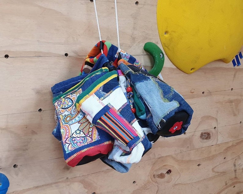 May include: A collection of colorful fabric scraps sewn together to create a unique and decorative hanging. The fabric scraps include paisley patterns, stripes, and denim.
