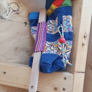 May include: A wooden shelf with a blue and colorful fabric bag hanging from it. The bag has a wooden dowel inside and a red bead on the drawstring. The shelf is made of wood and has a metal bracket attached to it.