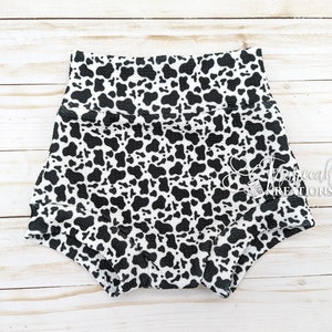 May include: Black and white cow print baby bloomers with a ruffled edge.