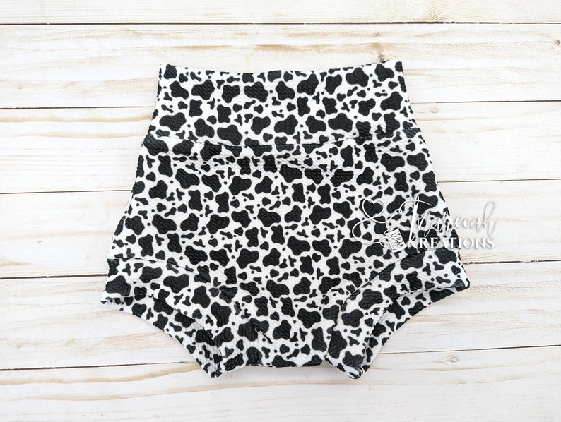 May include: Black and white cow print baby bloomers with a ruffled edge.