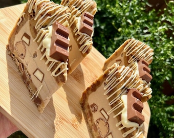 Puede incluir: Cuatro rebanadas de pastel de postre sobre una tabla de madera. El pastel tiene una base marrón claro con acentos blancos y marrones, cubierto con glaseado blanco y barras de chocolate. El postre se presenta en una tabla de cortar de bambú.