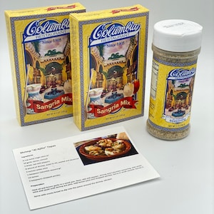 May include: Two yellow and blue boxes of Columbia Restaurant Sangria Mix, each with a picture of a courtyard and fountain. A small white jar of Columbia Restaurant All Purpose Seasoning with a yellow label and a picture of a courtyard and fountain. A recipe card for Shrimp "Al Ajillo" Tapas with a picture of shrimp in a dish.