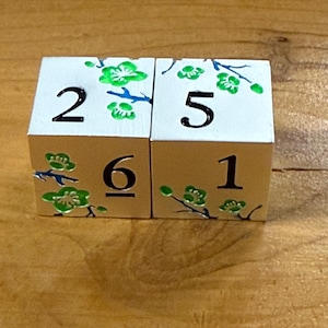 May include: Two white wooden dice with black numbers and green floral designs. The dice show the numbers 2, 5, 6, and 1. The floral designs are green with blue stems.
