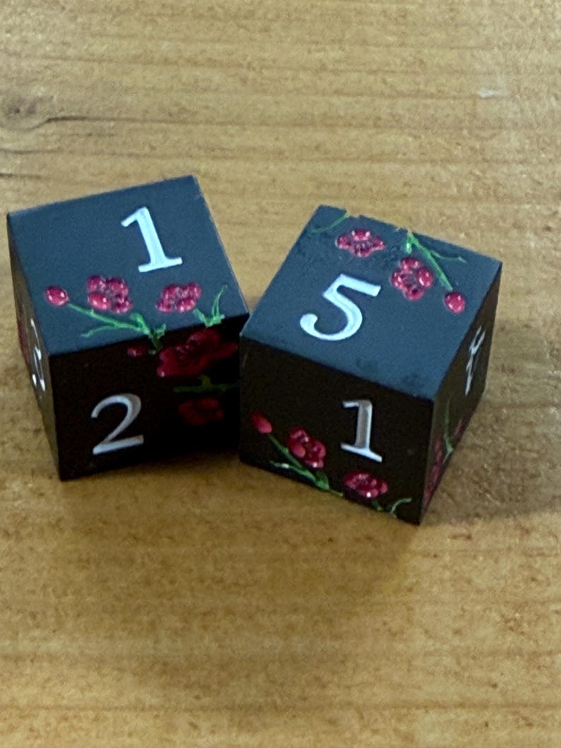 May include: Two black dice with white numbers and red floral accents. The dice show the numbers 1, 2, and 5. The dice are on a wooden surface.