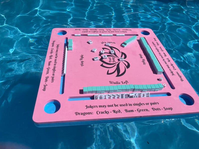 Puede incluir: Tablero de juego flotante rosa y azul con las palabras "Pool Jong" y "Walls Left" impresas en &eacute;l. El tablero tiene un dise&ntilde;o de flor de loto en el centro e instrucciones para jugar al juego.